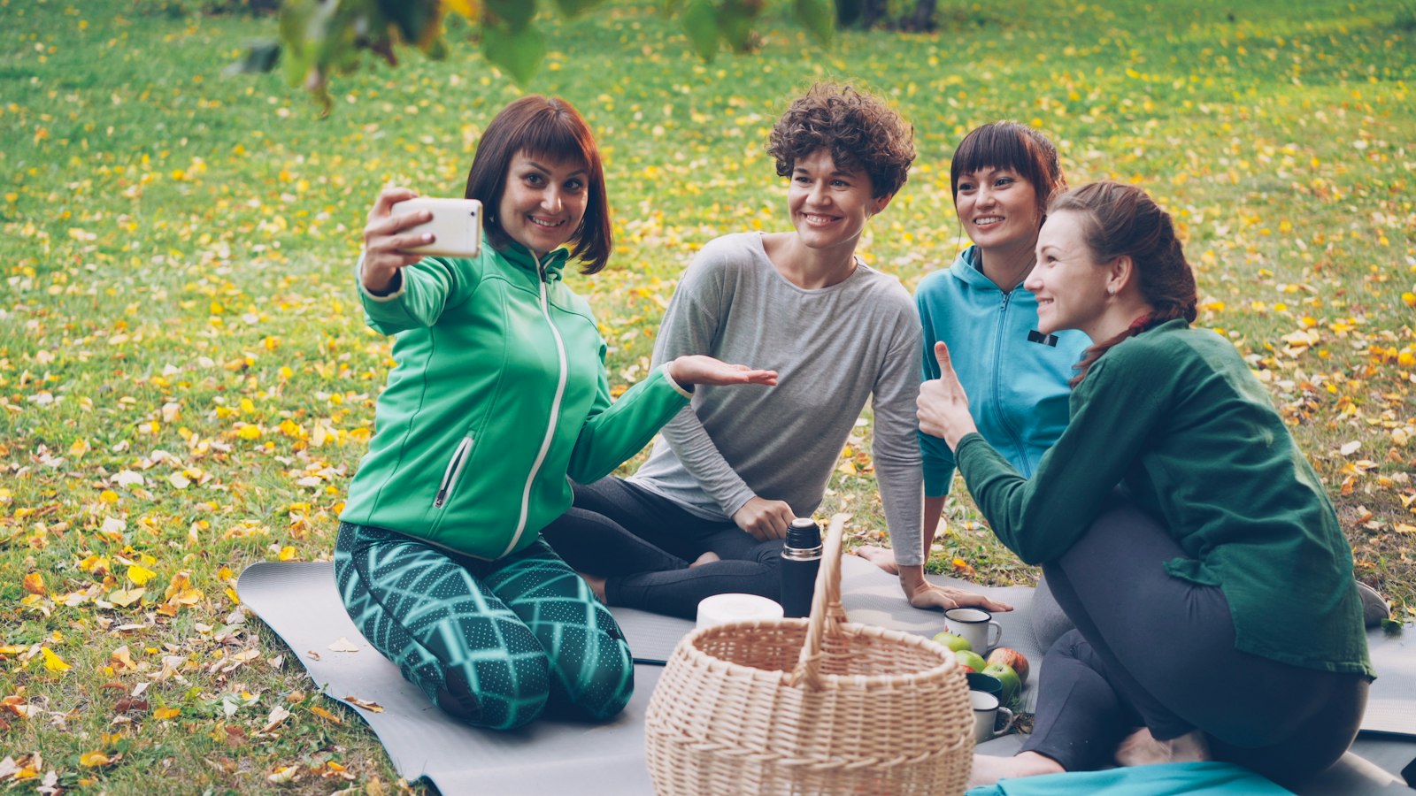 Four friends taking a selfie together on a picnic blanket in a park